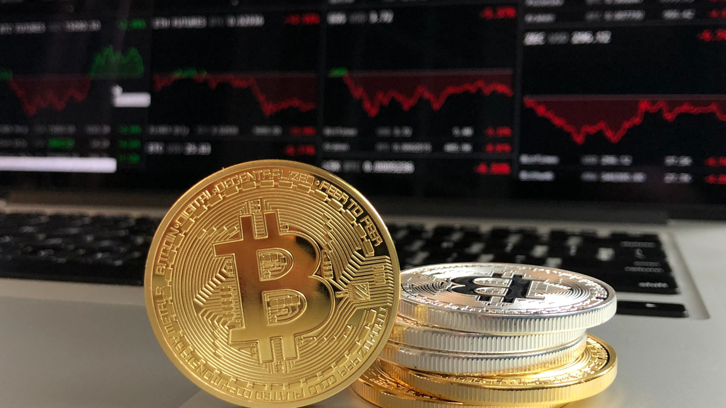 Gold and silver bitcoins in front of a trading chart on a computer screen